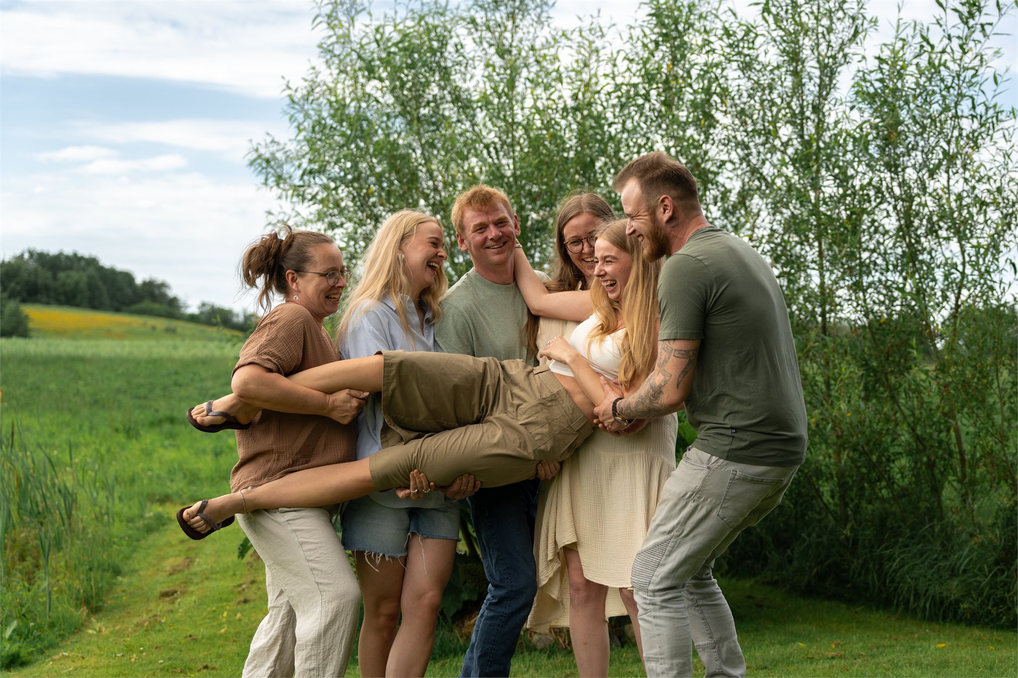 Gruppe venner der løfter en kvinde i et sommergrønt landskab